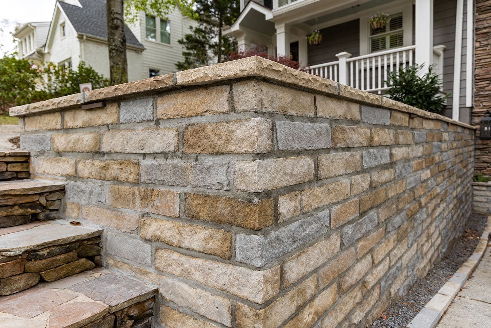A finished dry-laid stone retaining wall with a chiseled cap and flagstone steps, fronting a porch in Atlanta